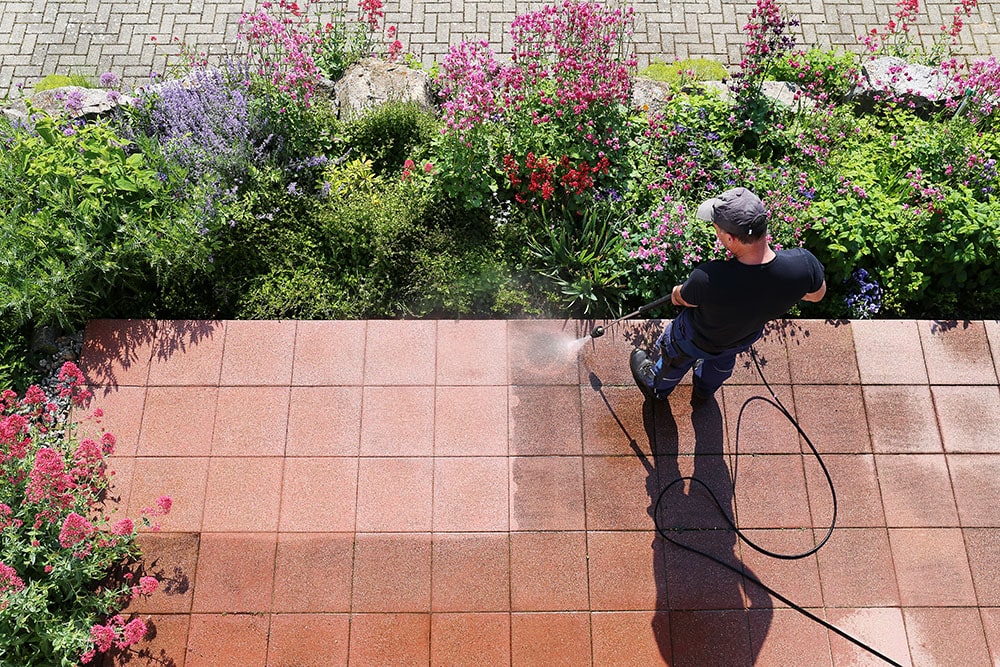 A Happy Valley Exteriors employee pressure washing a walkway near a flower garden