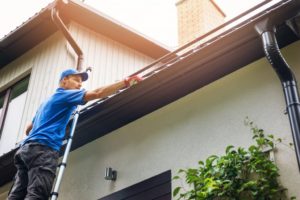 A gloved Happy Valley Exteriors service professional cleaning a gutter