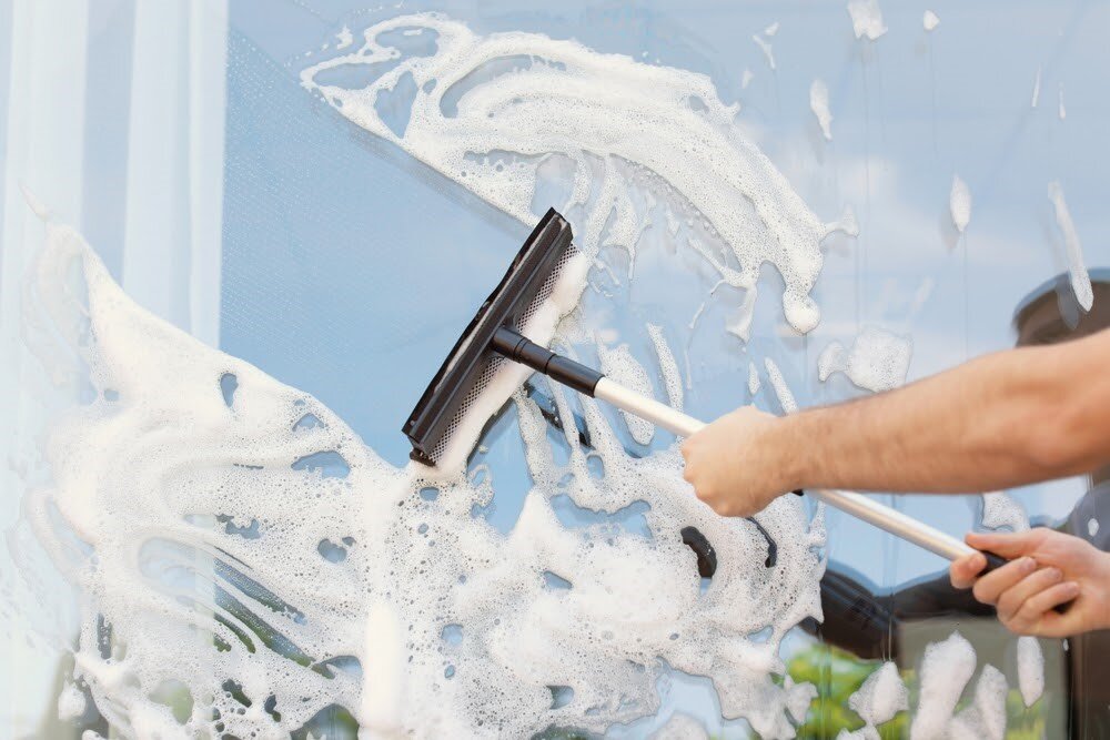 A window covered in soapy suds but being actively cleaned