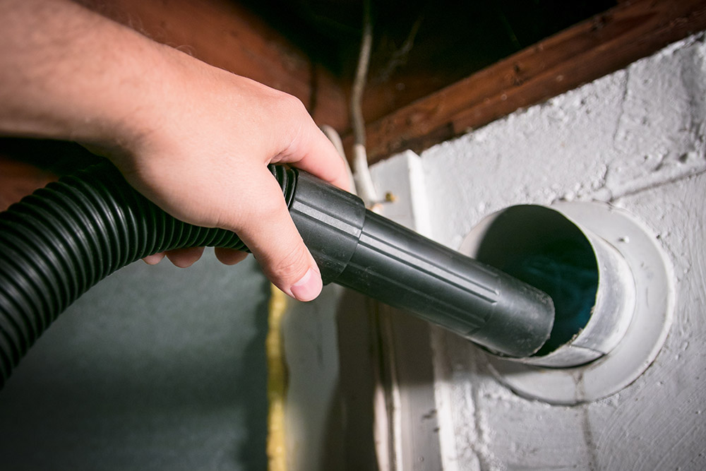 Using a vacuum to clean the back vents behind a dryer